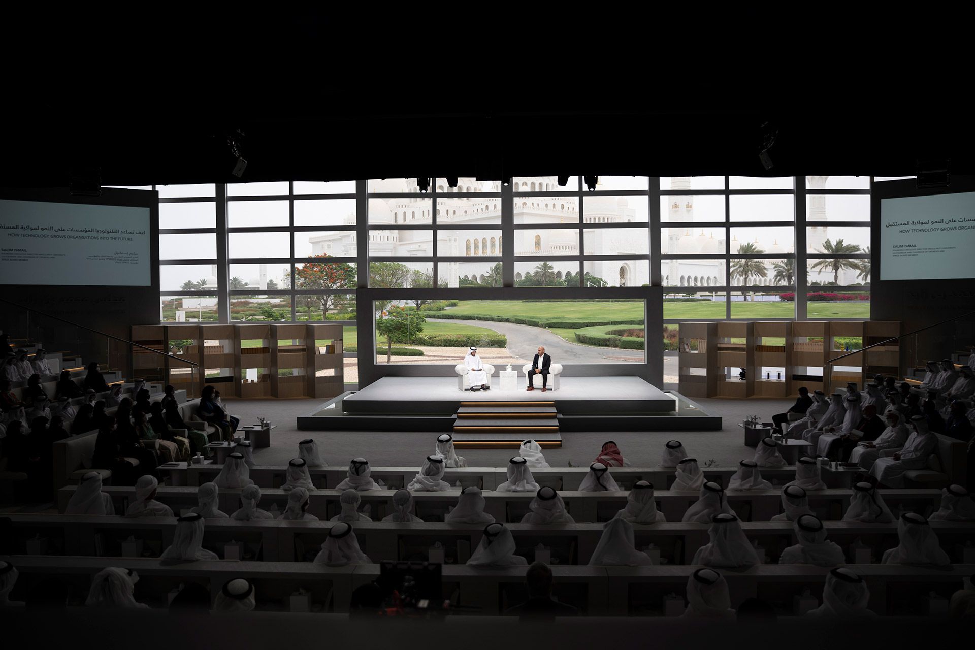 A Spark session in progress on a summit stage, two speakers in conversation before a full auditorium